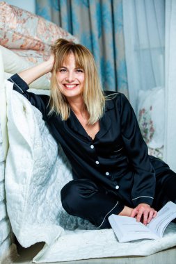 Genç güzel kadın ışık odada kirlenmiş. Rahat kadın pijamalar yatakta yatıyor. Günaydın kavramı - genç kadının uyanmanın mutlu gülümseme ile yüzünde.