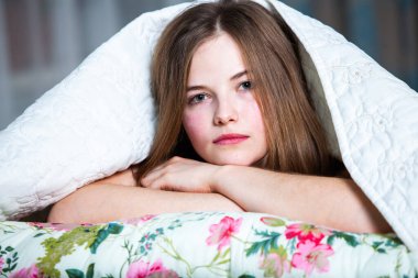 Genç, güzel, beyaz bir kadın aydınlık odada uyanıyor. Rahatlamış bir kadın yatakta uzanıp çay içiyor. Günaydın konsepti. Rus kız..