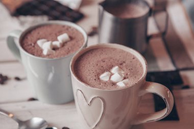 Two cups of hot cocoa with marshmallows and cinnamon sticks on wooden background. Love. Cocoa drink. Valentines day treat ideas.