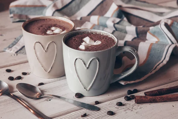 Two cups of hot cocoa with marshmallows and cinnamon sticks on wooden background. Love. Cocoa drink. Valentines day treat ideas.