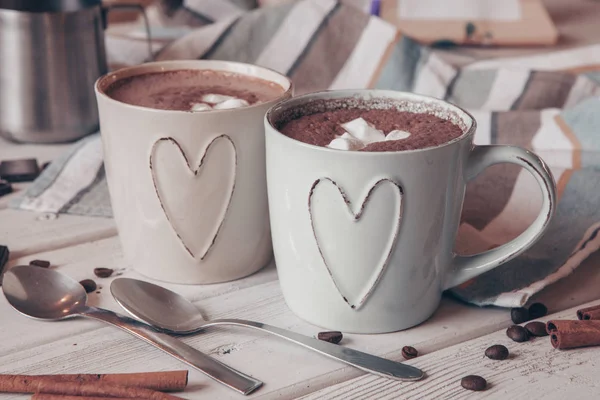 Two cups of hot cocoa with marshmallows and cinnamon sticks on wooden background. Love. Cocoa drink. Valentines day treat ideas.