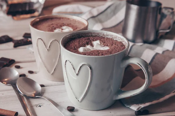 Two cups of hot cocoa with marshmallows and cinnamon sticks on wooden background. Love. Cocoa drink. Valentines day treat ideas.