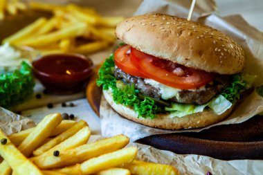 big tasty burger on a wooden table and french fries. Delicious burger with beef, tomato, cheese and lettuce.