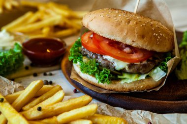 big tasty burger on a wooden table and french fries. Delicious burger with beef, tomato, cheese and lettuce.