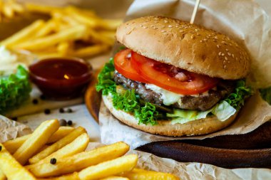 big tasty burger on a wooden table and french fries. Delicious burger with beef, tomato, cheese and lettuce.