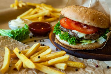 big tasty burger on a wooden table and french fries. Delicious burger with beef, tomato, cheese and lettuce.