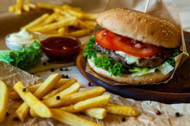 big tasty burger on a wooden table and french fries. Delicious burger with beef, tomato, cheese and lettuce.