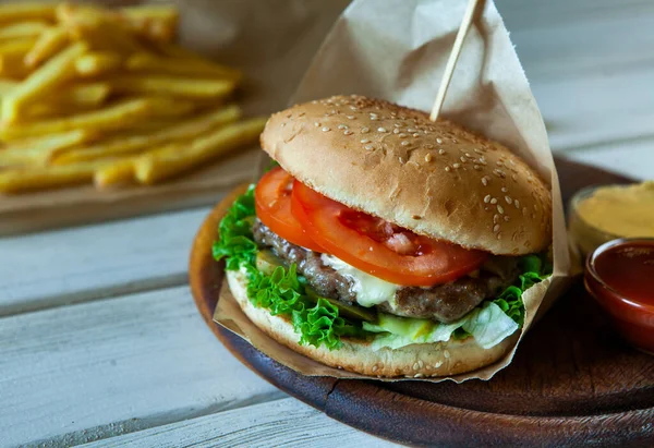 big tasty burger on a wooden table and french fries. Delicious burger with beef, tomato, cheese and lettuce.