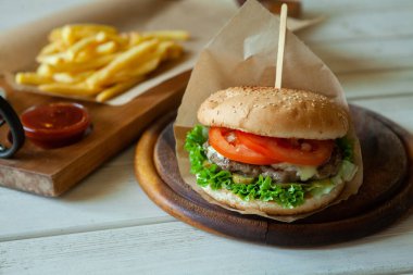 big tasty burger on a wooden table and french fries. Delicious burger with beef, tomato, cheese and lettuce.