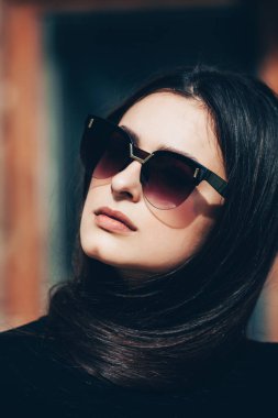 Uzun siyah saçlı, güneş gözlüğü takan güzel esmer bir kızın güzel moda portresi. Doğal ciltli güzel Rus kız suratı. Avrupa cazibesi. Güneş gözlüklü güzel hippi kız..