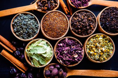 Tahta kasede çeşitli kurutulmuş çay yaprakları. Kurutulmuş bitki çayı yaprakları kapanıyor. Sağlıklı çay yapmak için farklı bitkiler ve çiçekler..