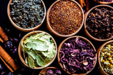 Tahta kasede çeşitli kurutulmuş çay yaprakları. Kurutulmuş bitki çayı yaprakları kapanıyor. Sağlıklı çay yapmak için farklı bitkiler ve çiçekler..