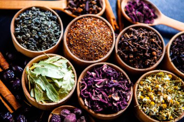 Tahta kasede çeşitli kurutulmuş çay yaprakları. Kurutulmuş bitki çayı yaprakları kapanıyor. Sağlıklı çay yapmak için farklı bitkiler ve çiçekler..