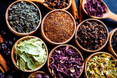 Tahta kasede çeşitli kurutulmuş çay yaprakları. Kurutulmuş bitki çayı yaprakları kapanıyor. Sağlıklı çay yapmak için farklı bitkiler ve çiçekler..