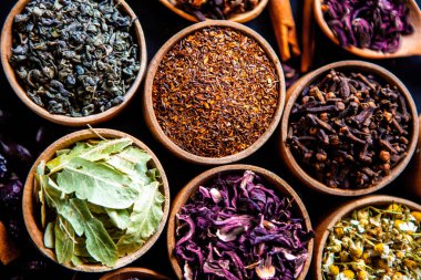 Tahta kasede çeşitli kurutulmuş çay yaprakları. Kurutulmuş bitki çayı yaprakları kapanıyor. Sağlıklı çay yapmak için farklı bitkiler ve çiçekler..