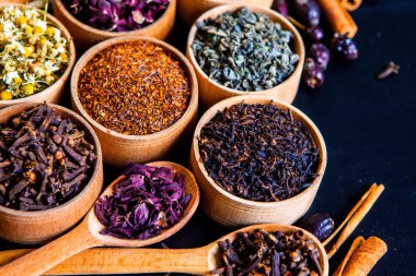 Tahta kasede çeşitli kurutulmuş çay yaprakları. Kurutulmuş bitki çayı yaprakları kapanıyor. Sağlıklı çay yapmak için farklı bitkiler ve çiçekler..