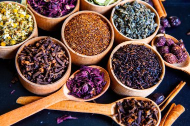 Tahta kasede çeşitli kurutulmuş çay yaprakları. Kurutulmuş bitki çayı yaprakları kapanıyor. Sağlıklı çay yapmak için farklı bitkiler ve çiçekler..