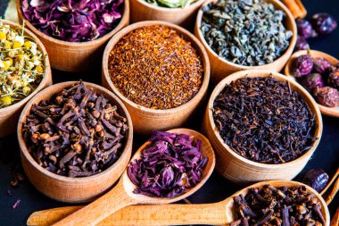 Tahta kasede çeşitli kurutulmuş çay yaprakları. Kurutulmuş bitki çayı yaprakları kapanıyor. Sağlıklı çay yapmak için farklı bitkiler ve çiçekler..