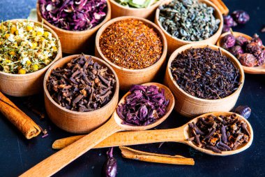 Tahta kasede çeşitli kurutulmuş çay yaprakları. Kurutulmuş bitki çayı yaprakları kapanıyor. Sağlıklı çay yapmak için farklı bitkiler ve çiçekler..