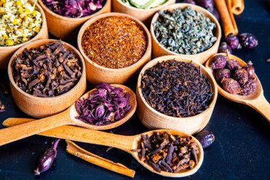 Tahta kasede çeşitli kurutulmuş çay yaprakları. Kurutulmuş bitki çayı yaprakları kapanıyor. Sağlıklı çay yapmak için farklı bitkiler ve çiçekler..