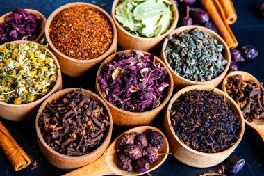 Tahta kasede çeşitli kurutulmuş çay yaprakları. Kurutulmuş bitki çayı yaprakları kapanıyor. Sağlıklı çay yapmak için farklı bitkiler ve çiçekler..