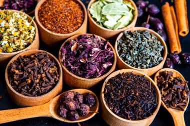 Tahta kasede çeşitli kurutulmuş çay yaprakları. Kurutulmuş bitki çayı yaprakları kapanıyor. Sağlıklı çay yapmak için farklı bitkiler ve çiçekler..