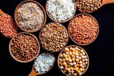 Bir kase mısır gevreği. Çeşitli doğal tahıl ve tahıllar. Siyah arka planda kaselerdeki farklı Groats tipleri. Sağlıklı besin.