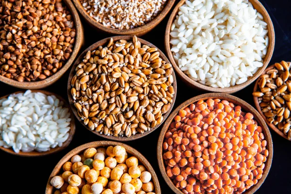 Bowls of various cereals. Various kinds of natural grains and cereals. Different types of groats in bowls on a black background. Healthy nutrition food