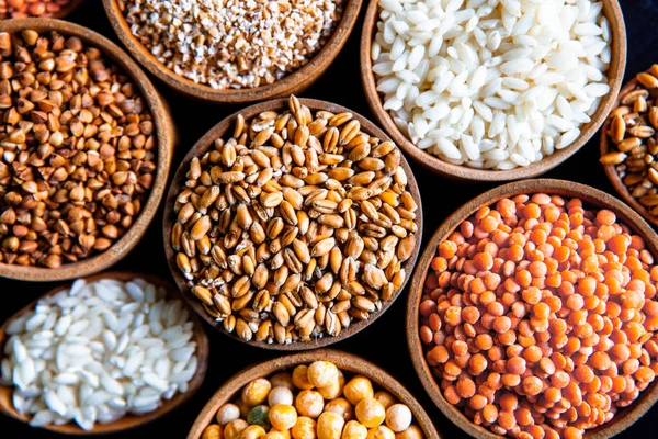 Bowls of various cereals. Various kinds of natural grains and cereals. Different types of groats in bowls on a black background. Healthy nutrition food