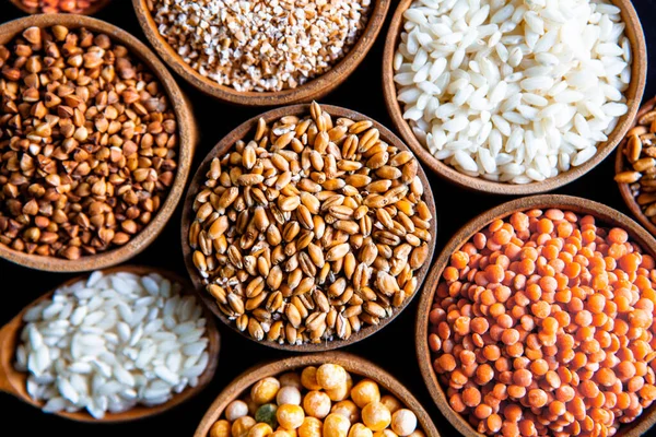 Bowls of various cereals. Various kinds of natural grains and cereals. Different types of groats in bowls on a black background. Healthy nutrition food