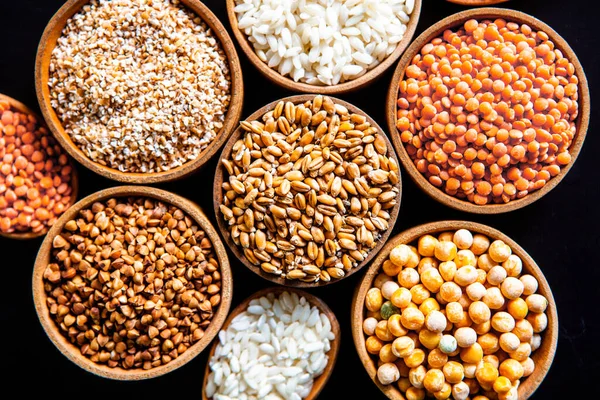 Bowls of various cereals. Various kinds of natural grains and cereals. Different types of groats in bowls on a black background. Healthy nutrition food