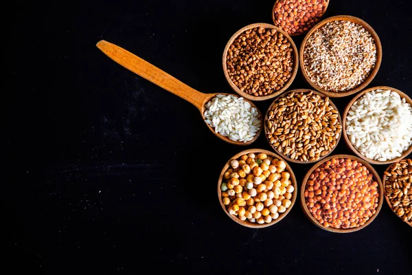 Bowls of various cereals. Various kinds of natural grains and cereals. Different types of groats in bowls on a black background. Healthy nutrition food