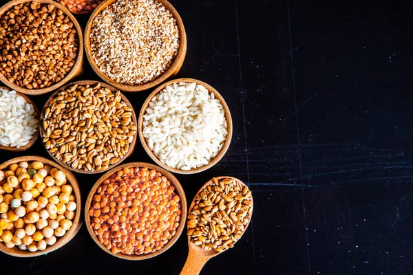 Bowls of various cereals. Various kinds of natural grains and cereals. Different types of groats in bowls on a black background. Healthy nutrition food