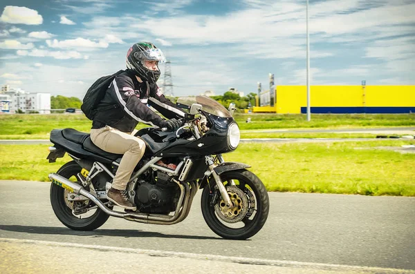 Ulyanovsk, Rússia - 10 de junho de 2017. Um motociclista em um capacete preto com uma mochila treina em uma motocicleta em uma pista de esportes . — Fotografia de Stock
