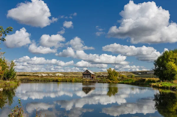 Photo of lonely wooden house on the lake, summer clouds against the backdrop of chalk hills.