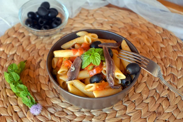 Deliciosa pasta italiana penne con anchoas en un tazón sobre una mesa . — Foto de Stock