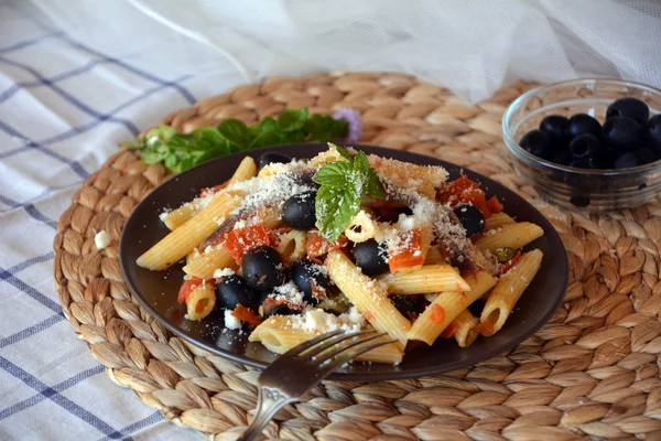 Delicious italian food penne ala puttanesca on a plate on a table. — Stock Photo, Image