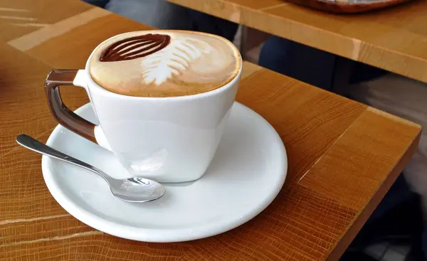 Filiżankę cappuccino spieniony na drewnianym stole. — Zdjęcie stockowe