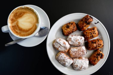 Lezzetli köpüklü cappuccino bir plaka üzerinde siyah bir arka plan üzerinde beyaz bir Kupası.