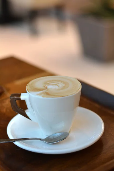 Delicioso capuchino espumoso en una taza blanca en un plato . — Foto de Stock