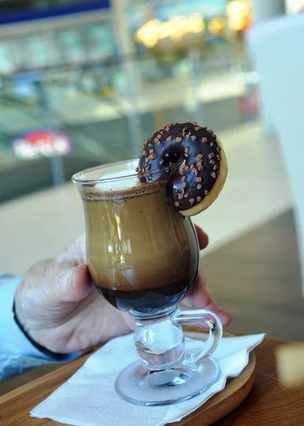 Caffè nero con latte su una tazza di vetro e piccola ciambella su un tavolo di legno . — Foto Stock