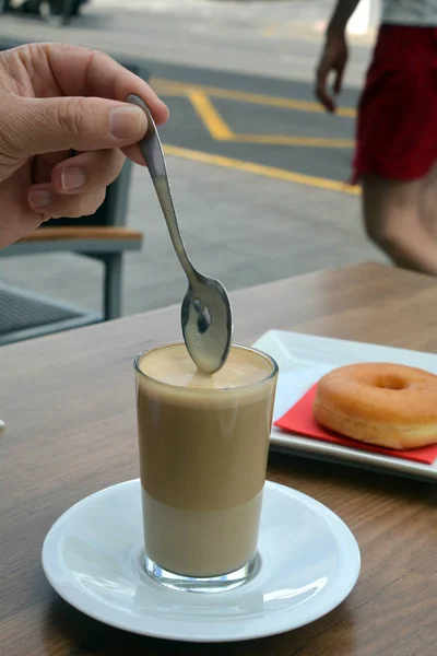 Man\'s hand stirring black coffee with spoon on a glass cup.