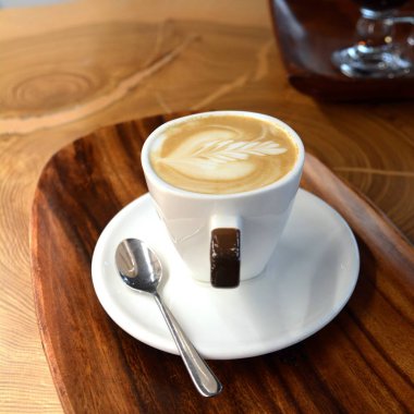 Ahşap bir masa üzerinde bir tabakta köpüklü kapuçino fincan.