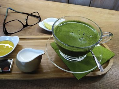 Sıcak sütle kibrit yeşil çay, cam bir bardakta, ahşap tabakta..