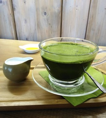 Sıcak sütle kibrit yeşil çay, cam bir bardakta, ahşap tabakta..