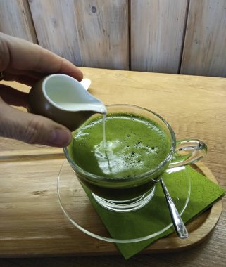 Sıcak sütle kibrit yeşil çay, cam bir bardakta, ahşap tabakta..