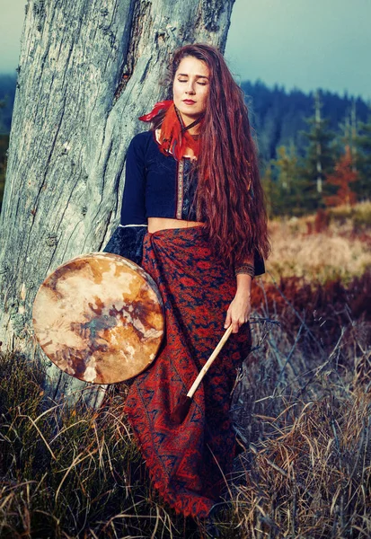 Bela garota xamânica jogando no tambor quadro xamã na natureza. — Fotografia de Stock