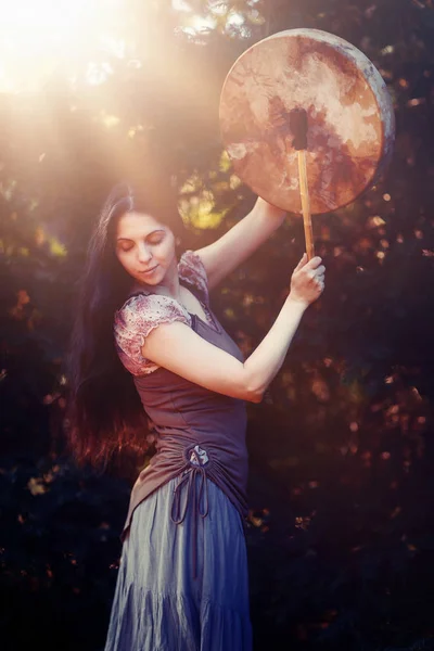 Beautiful shamanic girl playing on shaman frame drum in the nature. — Stock Photo, Image