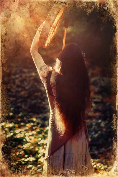 Beautiful shamanic girl playing on shaman frame drum in the nature, old photo effect. — Stock Photo, Image