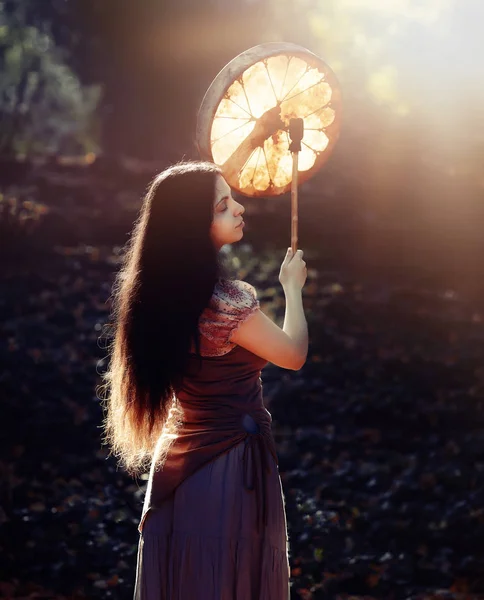 Beautiful shamanic girl playing on shaman frame drum in the nature. — Stock Photo, Image